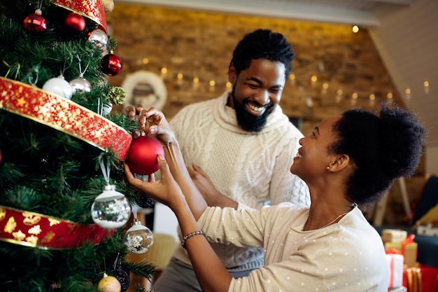 Glückliches schwarzes Paar, das sich beim Schmücken des Weihnachtsbaums zu Hause unterhält