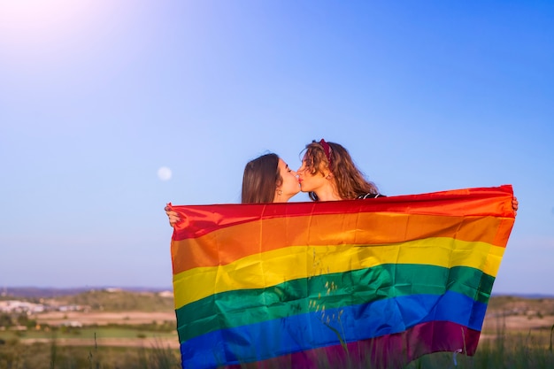 Glückliches schwules Mädchenpaar küsst vor schwuler Flagge