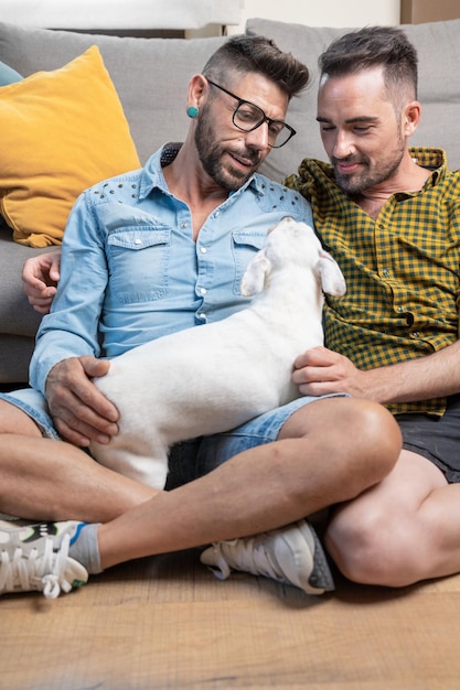 Glückliches schwules Paar, das auf dem Boden sitzt und zu Hause mit dem Hund spielt