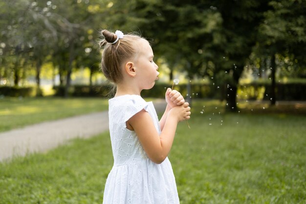 glückliches süßes Kind Mädchen bläst Dendelion Blume im grünen Park