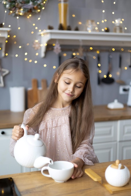 glückliches süßes kleines Mädchen in schönem Kleid bereitet Tee vor Weihnachtsmorgen in der Küche Weihnachtsfamilie Harmonie Weihnachtskind in der Küche