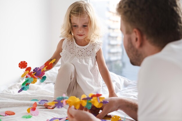 Foto glückliches süßes weißes zweijähriges kleinkind, das mit einem erwachsenen mann mit farbenfrohen spielzeugkreisen spielt