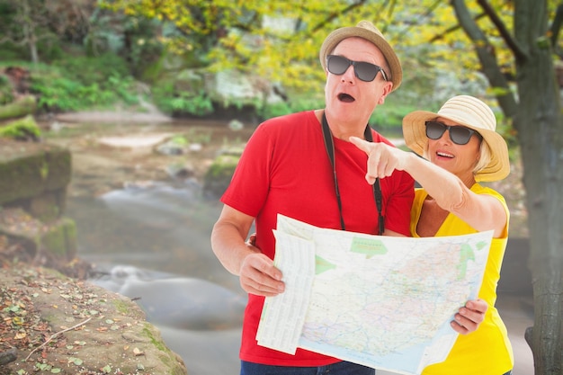 Glückliches Touristenpaar, das eine Karte gegen Stromschnellen verwendet, die entlang des Waldes fließen