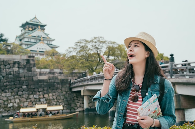 Glückliches touristisches asiatisches Mädchen, das Papierkarte hält