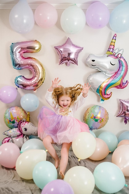 Glückliches und überraschtes Mädchen feiert ihren Geburtstag Partydeko mit Luftballons im Stil Einhorn Regenbogen mein kleines Pony Geburtstagsparty seit 5 Jahren Idee zur Partydeko