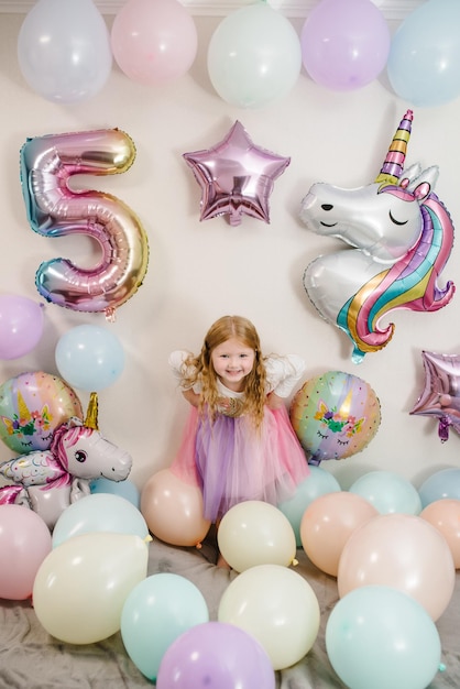 Glückliches und überraschtes Mädchen feiert ihren Geburtstag Partydeko mit Luftballons im Stil Einhorn Regenbogen mein kleines Pony Geburtstagsparty seit 5 Jahren Idee zur Partydeko