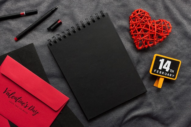 Glückliches Valentinstagkonzept, Schwarzbuch, rotes Herz und Stift auf grauem Stoff