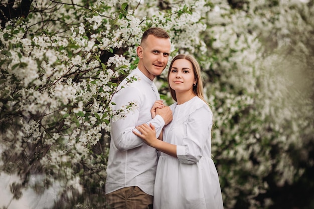 Glückliches verliebtes Familienpaar in einem frühlingsblühenden Apfelgarten. Glückliche Familie genießt einander beim Spaziergang im Garten. Der Mann hält die Hand der Frau. Familienbeziehungen