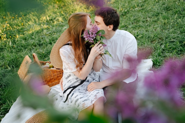 Glückliches verliebtes Paar auf einem Picknick, das sich nah oben mit lila Frühlingsflieder küsst