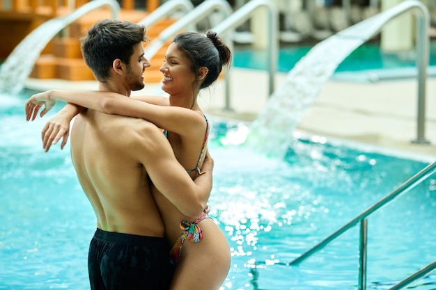 Glückliches verliebtes Paar, das im Schwimmbad des Spas umarmt steht
