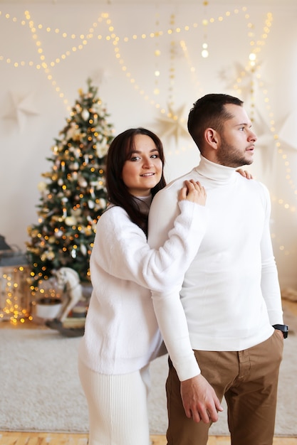 Glückliches Weihnachtskonzept, verliebtes Paar, das durch den Weihnachtsbaum umarmt und küsst