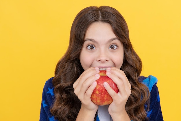 Glückliches zahniges Kindermädchen beißt frischen Apfel im kuscheligen Bademantel, Kinderstomatologie.