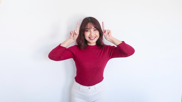 Glückliches Zeigen oben des asiatischen schönen Mädchens mit rotem Hemd im weißen Hintergrund