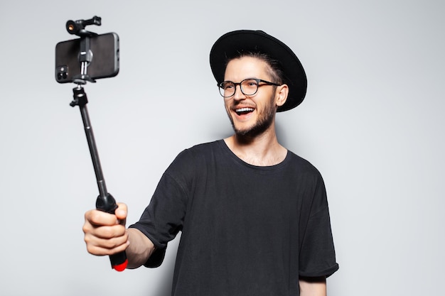 Glückskerl, der Video per Smartphone mit Selfie-Stick auf grauem Hintergrund macht