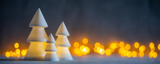 Glühende Weihnachtsbäume aus weißer Keramik auf dem Hintergrund von Bokeh-Lichtern Geringe Schärfentiefe