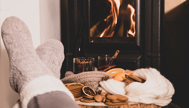 Glühwein am Kamin, 2 Gläser Getränk, Gewürze, ein warmer Schal und Füße in warmen Socken in der Nähe des Ofens