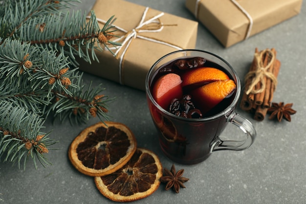 Glühwein, ein Geschenk und Gewürze auf dem Tisch neben dem Baum