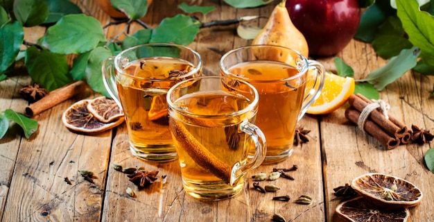 Glühwein Glas Tassen Apfel Birne und Orange aromatisierter heißer Apfelwein mit Gewürzen Fermentiertes Cocktail-Fruchtgetränk mit niedrigem Alkoholgehalt auf ustischem Holztisch Hintergrund mit Blättern