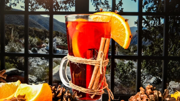 Glühwein Heißes Weihnachtsgetränk mit Gewürzen auf einer Fensterbank neben dem Fenster. Orangenscheiben, Zimtstangen, Tannenzapfen. Urlaubsatmosphäre, rustikaler Stil. Die Idee zum Erstellen von Grußkarten