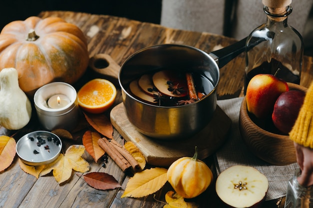 Glühwein-Heißgetränk mit Zitrusfrüchten, Äpfeln und Gewürzen im Aluminiumtopf auf Holz