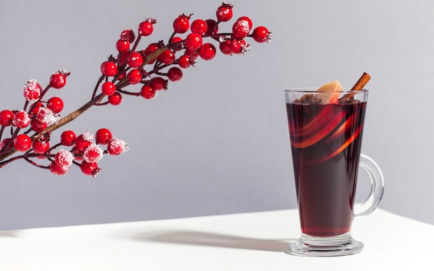 Glühwein im glas mit einer zimtstange mit roten winterbeeren trendig das foto mit...