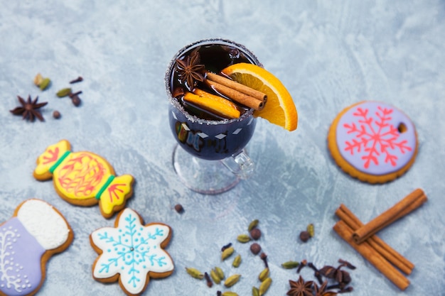 Glühwein im glasbecher mit gewürzen. heißes weihnachtsgetränk mit dekoriertem neujahrs-ingwerbrot auf grauem steintisch. draufsicht.