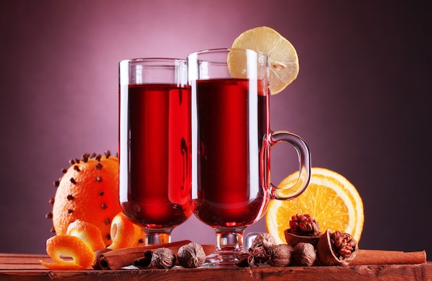 Glühwein in den Gläsern, Gewürz und Orange auf Holztisch auf violettem Hintergrund