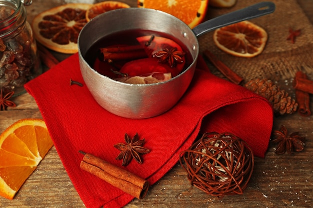 Glühwein in Schmorpfanne auf mit roter Serviette, Zimt und orangefarbenem Holzhintergrund dekoriert