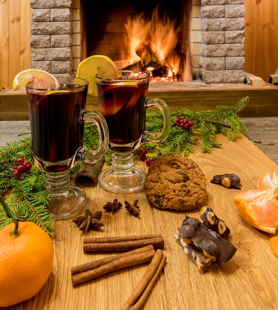 Glühwein in Trinkgläsern und Weihnachtsdekorationen vor gemütlichem Kamin.