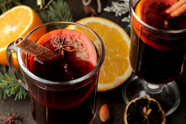 Glühwein mit Zimt und Orange in Glasbechern Nahaufnahme und Weihnachtsschmuck auf dunklem Hintergrund. Weihnachten. Neujahr.