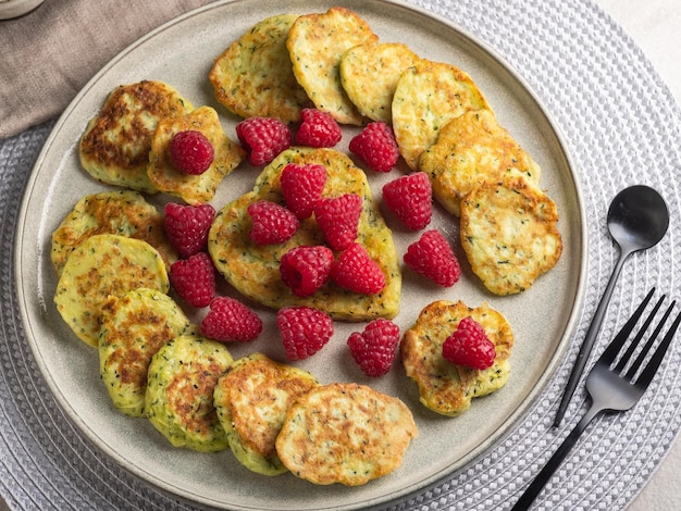 Glutenfreie Zucchini-Pfannkuchen mit frischen Himbeeren, Himbeermarmelade, Sauerrahm auf einem grauen Teller