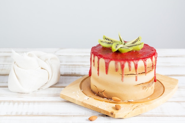 Foto glutenfreier kuchen mit erdbeerglasur, kokosnusschips und mandeln auf einem ständer auf einem holztisch