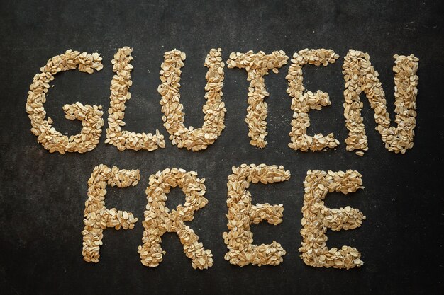 Glutenfreies Wort geschrieben mit Getreide auf dunklem Hintergrund Konzept des gesunden Lebensstils glutenfrei