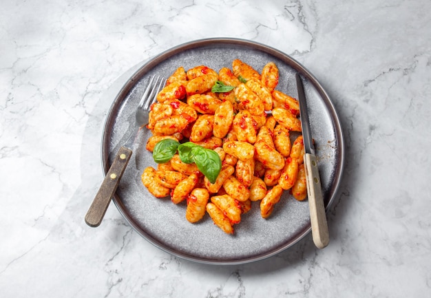 Gnocchi de patata tradicional italiana con salsa de tomate y albahaca fresca sobre placa gris mármol procedencia