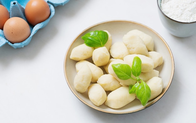 Gnocci de patata italiano tradicional decorado con hojas de albahaca, huevos, harina. Concepto crudo.