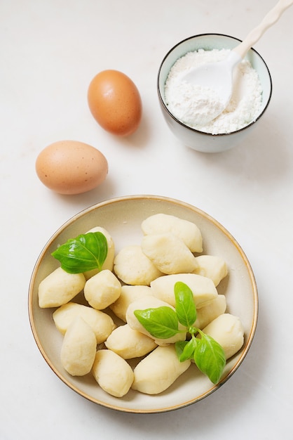 Gnocci de patata italiano tradicional decorado con hojas de albahaca, huevos, harina. Vista superior. Lay Flat