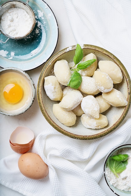 Gnocci de patata italiano tradicional (pasta) decorado con hojas de albahaca, huevos, harina. Concepto de pasta cruda. Vista superior. Lay Flat