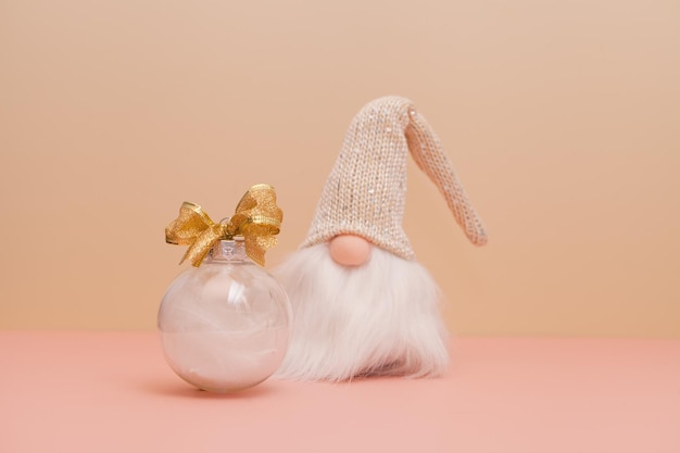 Gnomo y bola de navidad sobre fondo rosa decoraciones modernas con plumas blancas regalos de año nuevo