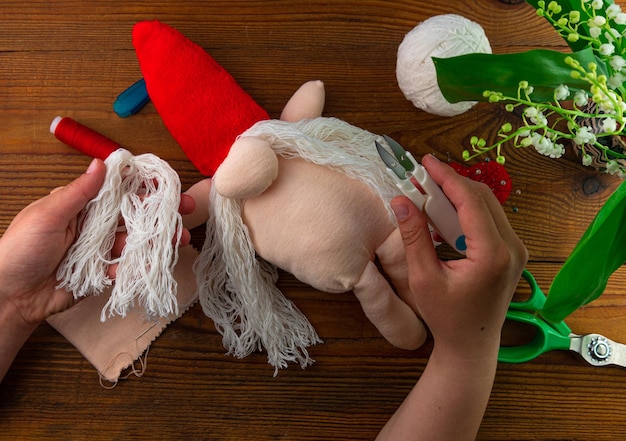 Foto gnomo escandinavo fazendo passo a passo tutorial artesanal fundo de madeira tecido caseiro decoração de natal sueca diy hobby brinquedo de pelúcia macio costurado barba longa chapéu vermelho costura conceito hygge