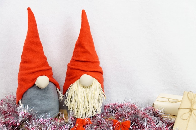 Gnomos de Navidad caseros sobre fondo blanco y madera rodeado de brillantes adornos navideños, con espacio de copia.