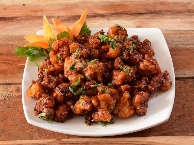 Gobi Manchurian Popular comida indochinesa feita de floretes de couve-flor servidos em um prato branco sobre uma mesa de madeira rústica foco seletivo