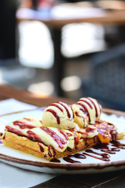 Gofre belga con salsa de helado de bayas y frutas frescas en rodajas en un plato sobre una mesa de restaurante Imagen vertical de gofre belga de harina integral con una bola de helado y jarabe de bayas naturales