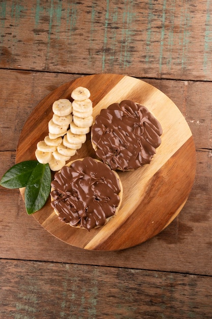 Gofre de crema de chocolate y avellanas con rodajas de plátano en una tabla de madera sobre un retrato de vista superior