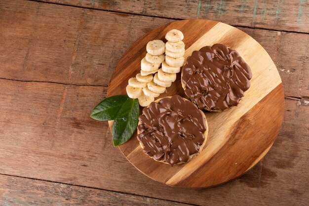 Gofre de crema de chocolate y avellanas con rodajas de plátano en tablero de madera sobre el paisaje de vista superior en primer plano