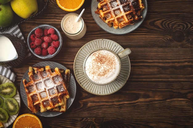 Gofres belgas, café, yogur, frutas y bayas en un fondo de madera, concepto de desayuno.