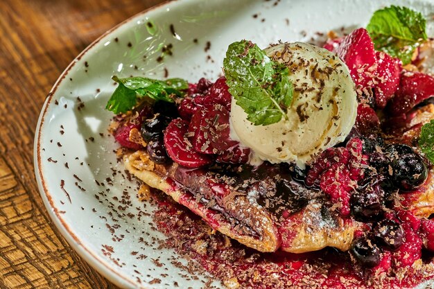 Gofres belgas con helado y fruta en un bol sobre fondo de madera