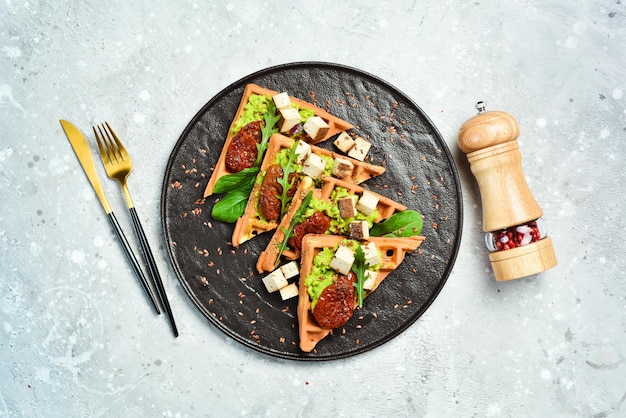 Gofres belgas con paté de aguacate, tomates secos y queso de tofu El concepto de alimentación saludable Sobre un fondo de piedra Vista superior