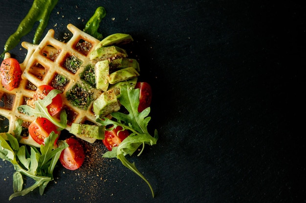 Gofres belgas recién horneados con rúcula, tomates y aguacate en un plato negro. Gofres salados. Concepto de desayuno. Desayuno saludable.