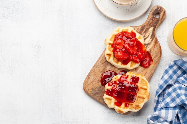 Gofres recién hechos para el desayuno con mermelada de bayas, café y naranja