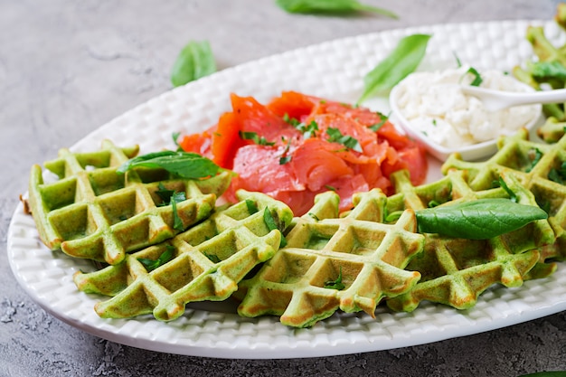 Gofres salados con espinacas y queso crema, salmón en plato blanco. Comida sabrosa.